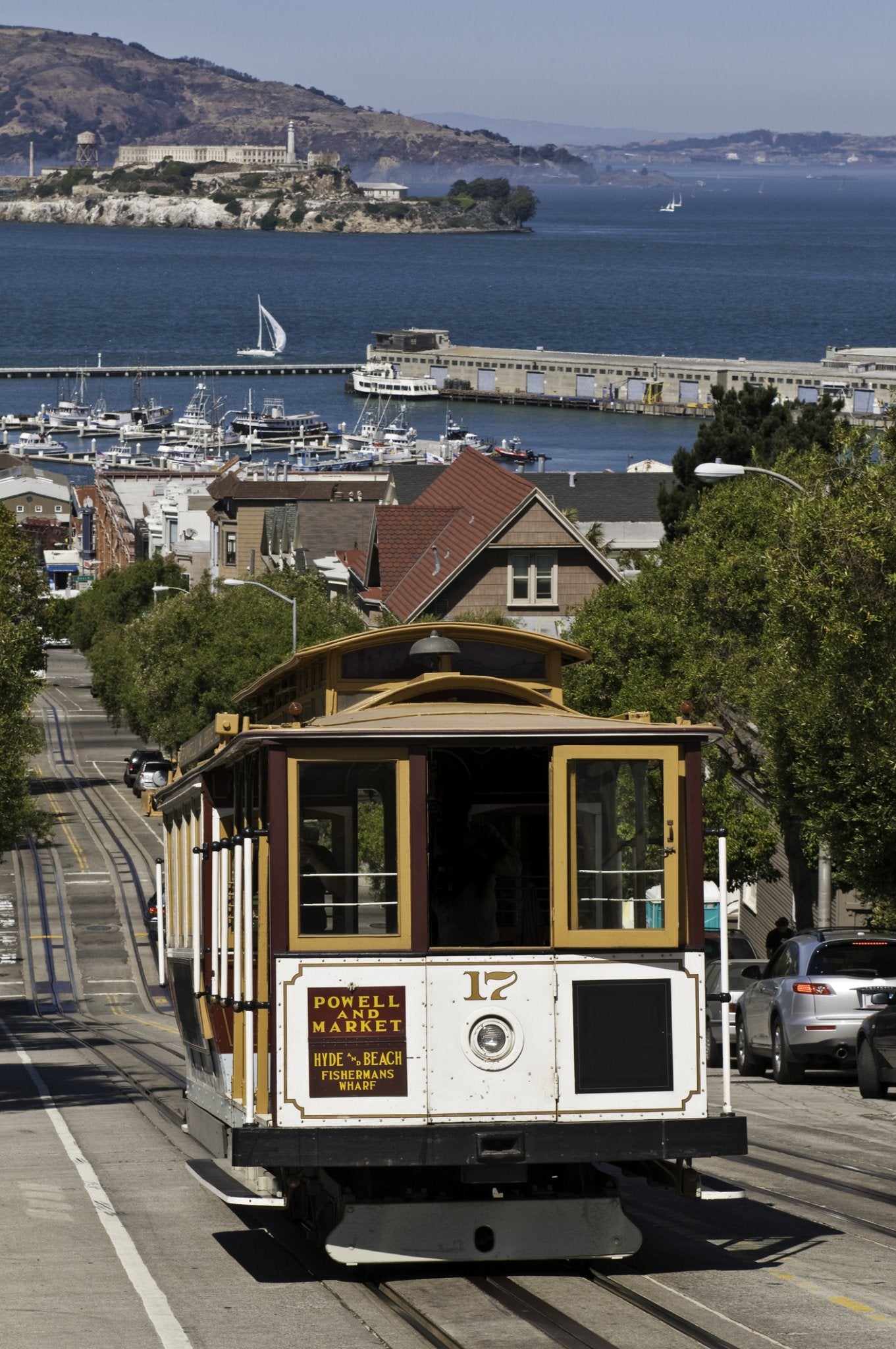 Cable car going up a steep street in San Francisco with the Bay and Alcatraz in the background